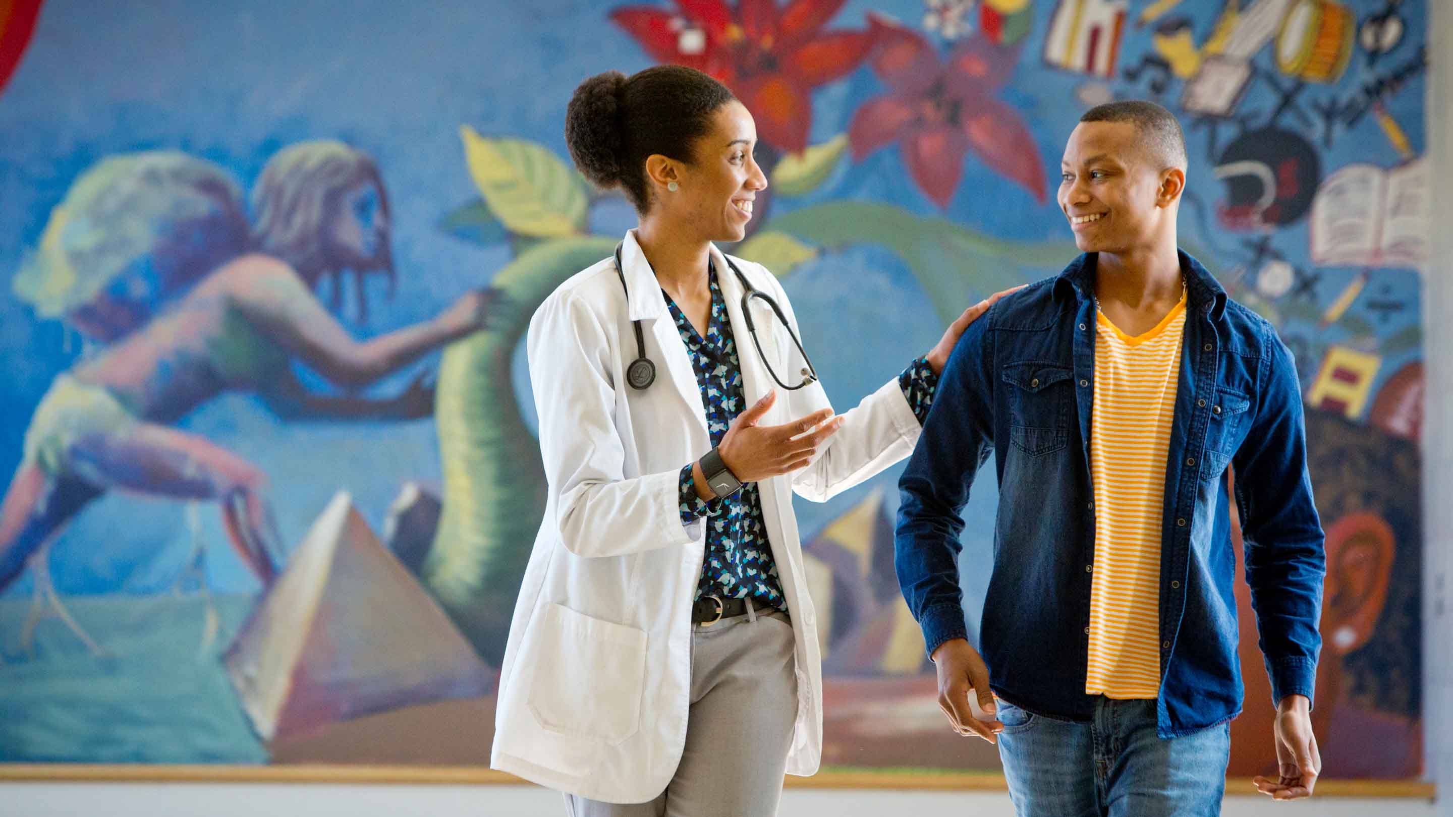 A doctor an patient joyfully talking in front of a colorful mural.