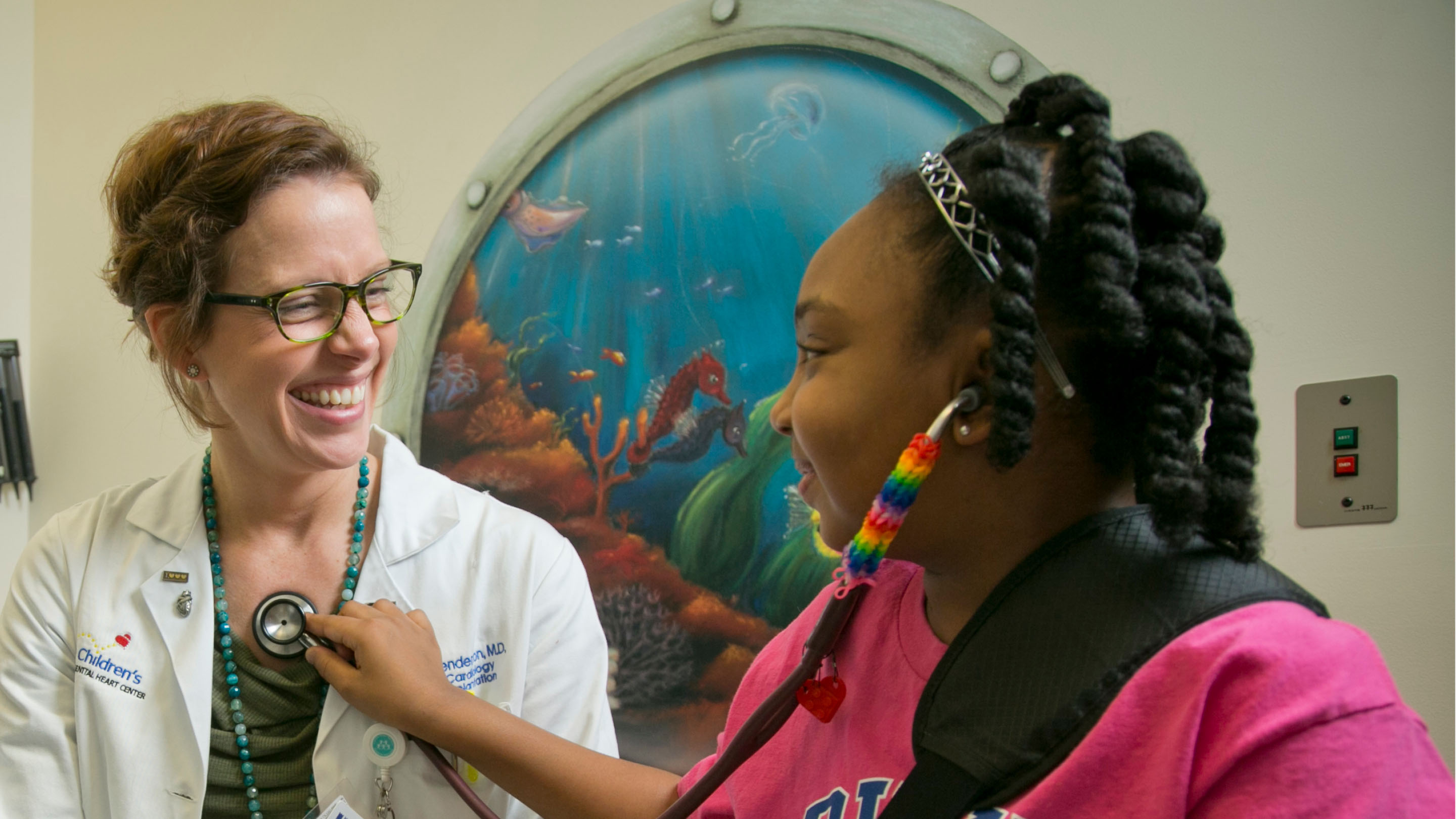 Student using a stethoscope on her doctor who is laughing.