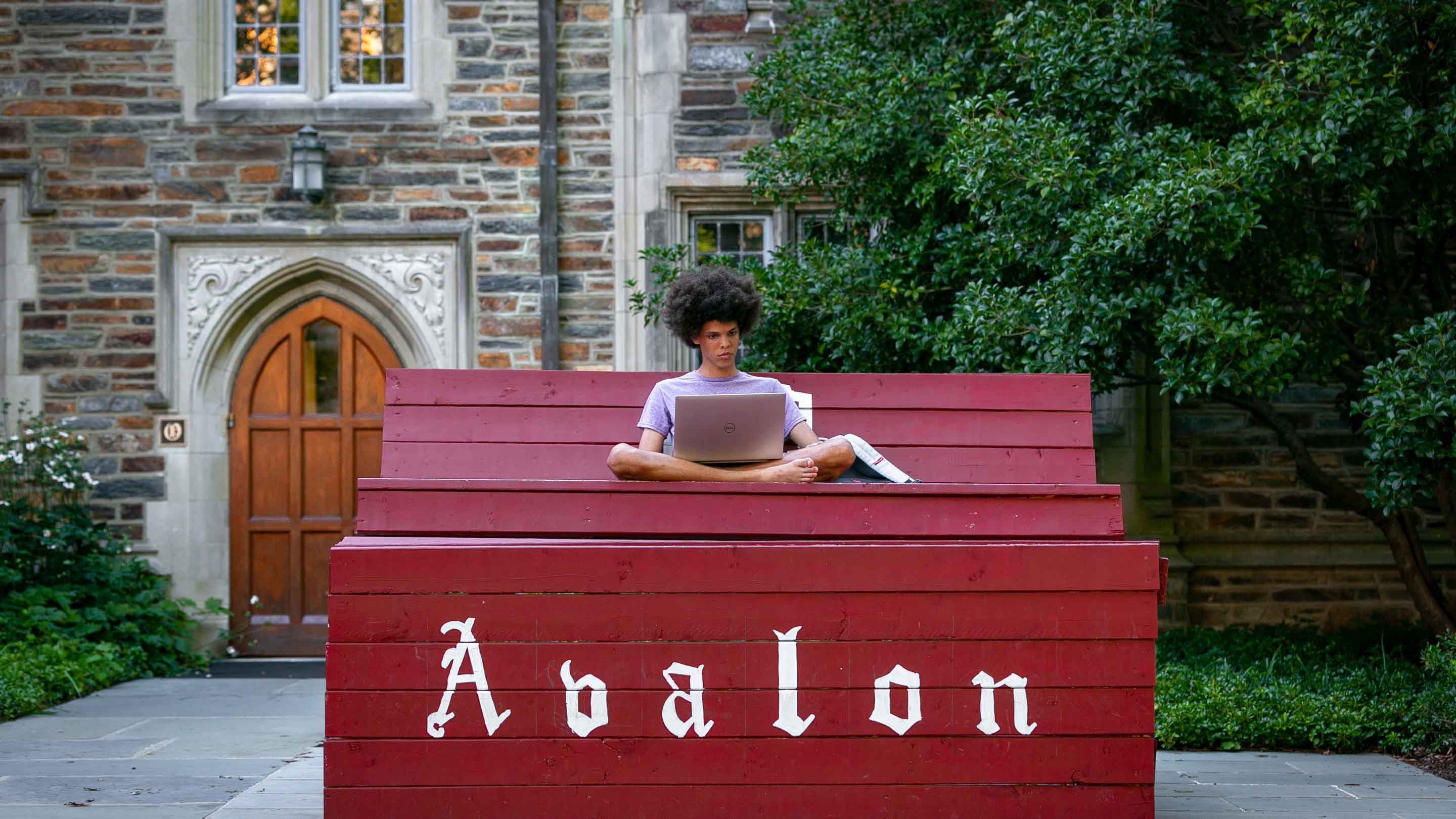 Person sitting with their laptop on a oversized red bench with "abalon" written on the front. 