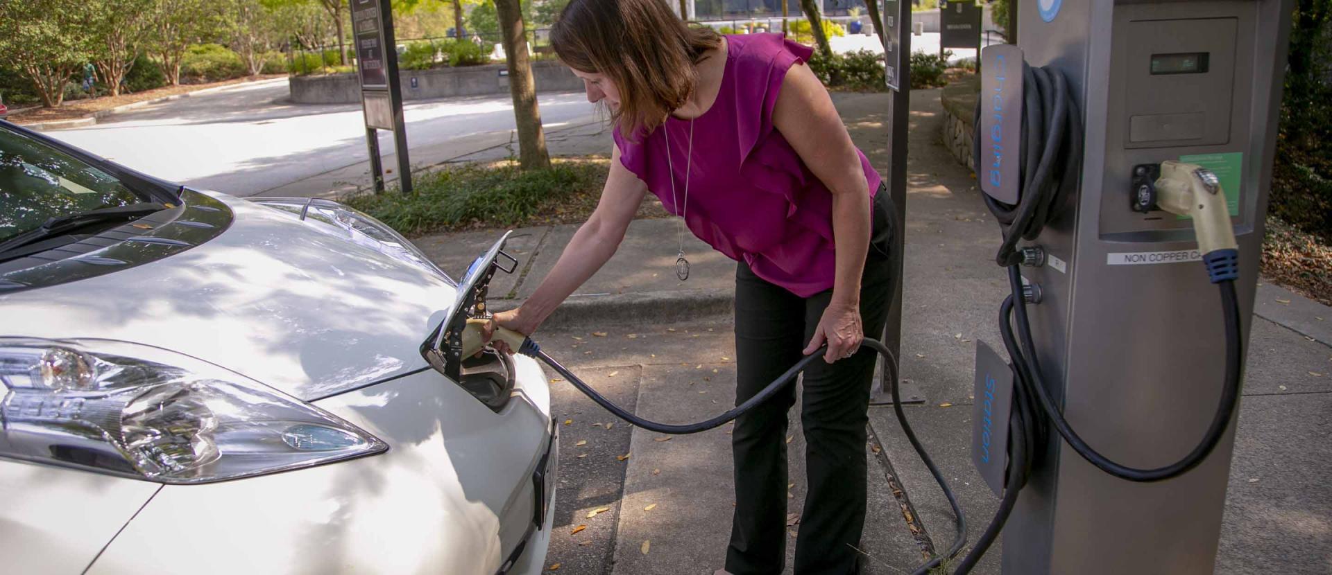 A woman charges an electric vehicle at a charging station.