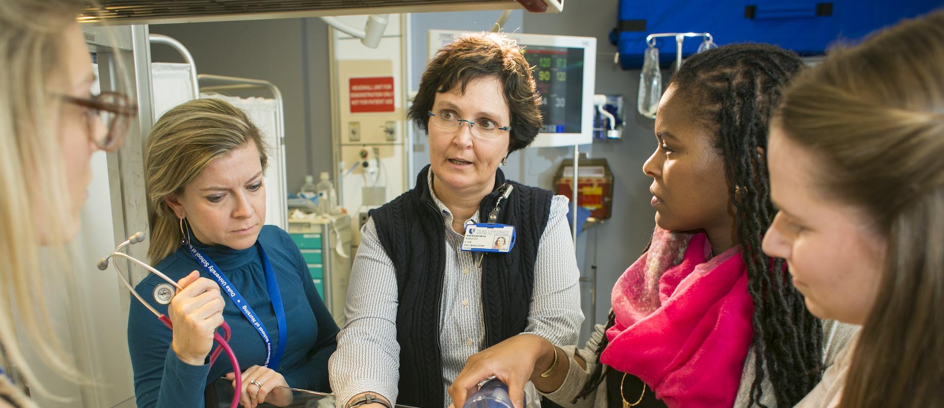 Students surround School of Nursing instructor teaching with a CPR manikin.