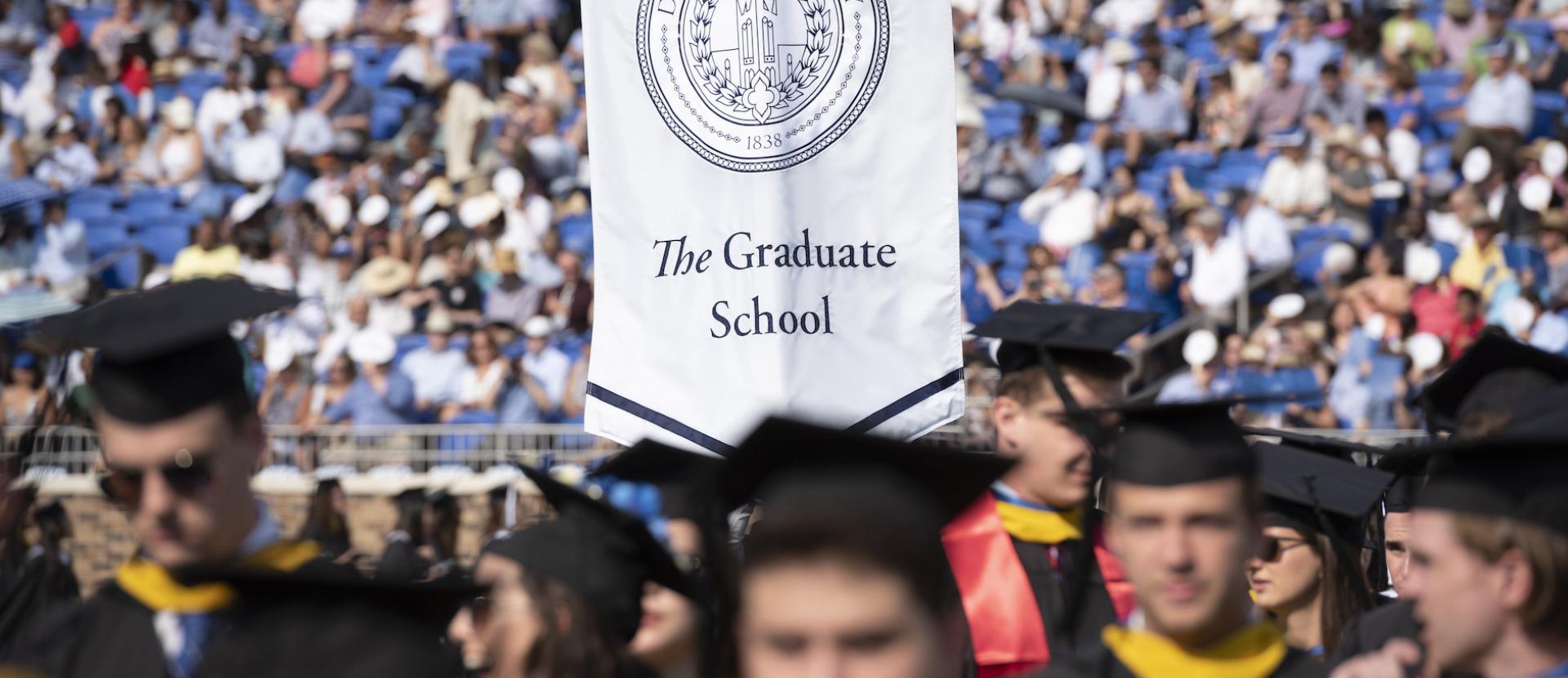 Graduate school banner at graduation in sea of graduates.