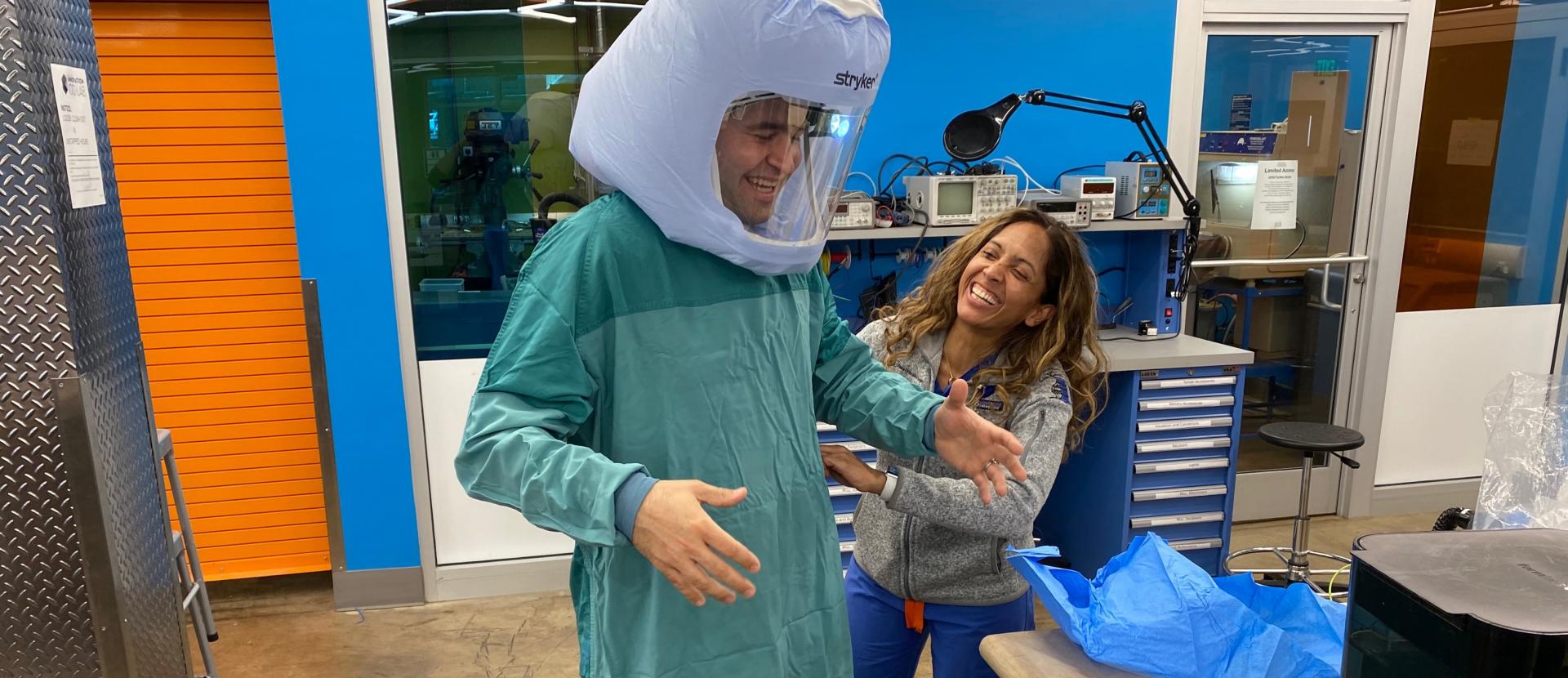 Professor Eric Richardson tries out the PAPR he helped design and produce with Dr. Melissa Erickson by his side.