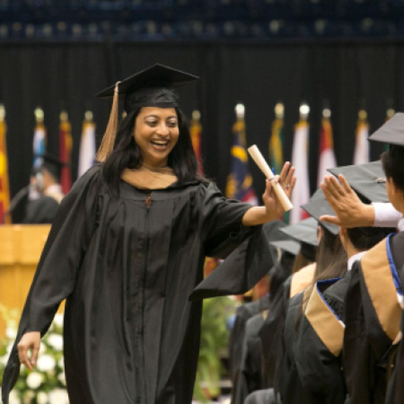 A woman high-fives an audience member after receiving her diploma.