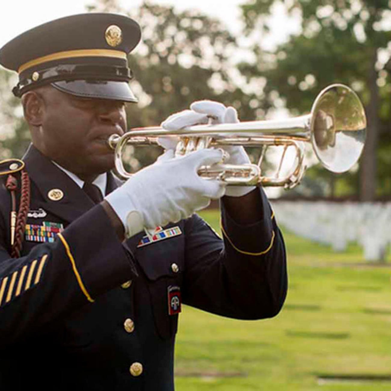 A man in a military uniform plays a trumpet in a graveyard.