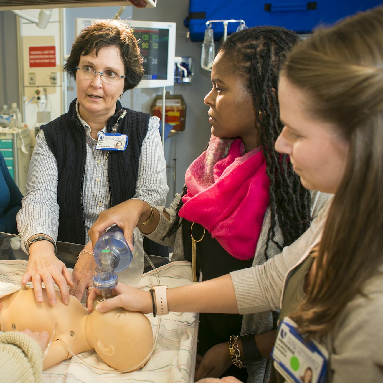 Students surround School of Nursing instructor teaching with a CPR manikin.