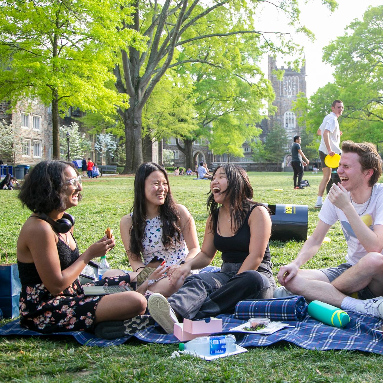 Four Duke students picnicking on a blanket on the campus Quad