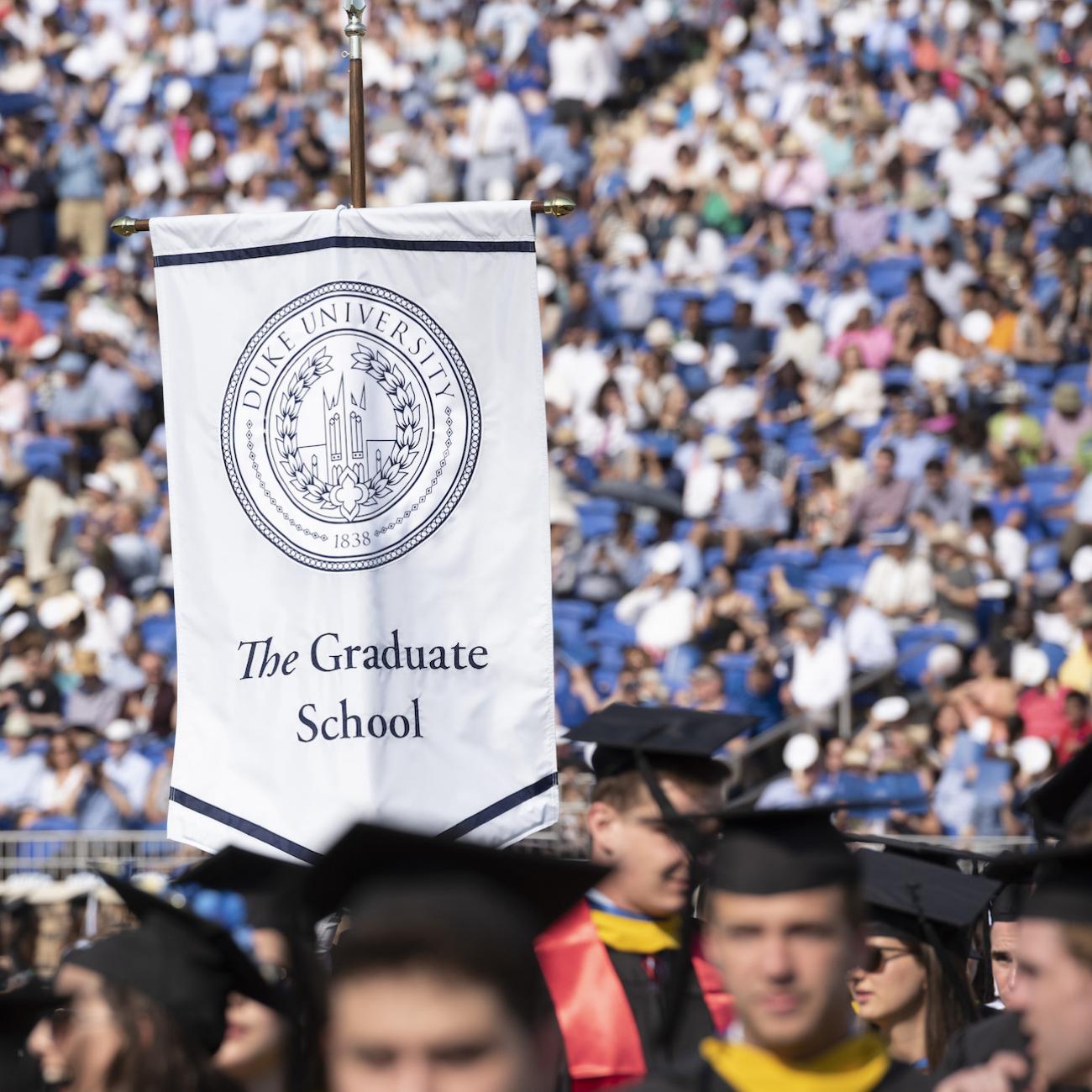Graduate school banner at graduation in sea of graduates.