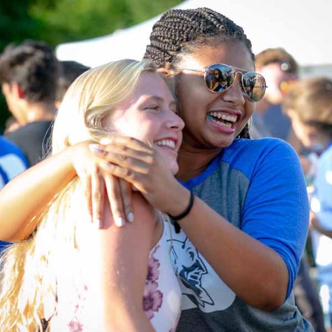 Two students hugging and laughing.