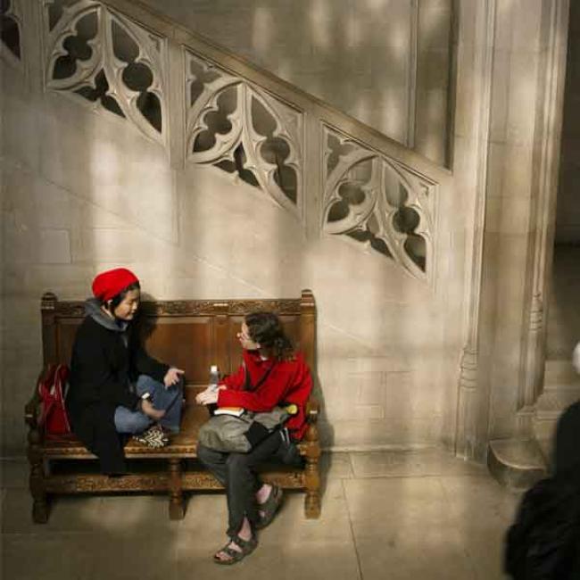 Two student talking on a bench surrounded by marble, with a staircase going up behind them.